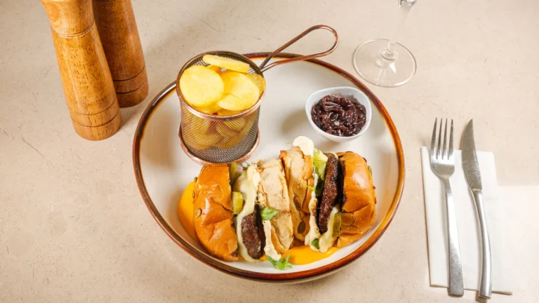 Burgerul Casei cu sos cheddar & cartofi – chiftea suculentă din carne de vită, sos cheddar cremos, ceapă caramelizată, roșii. Preparat servit la Restaurant Intim din Focșani