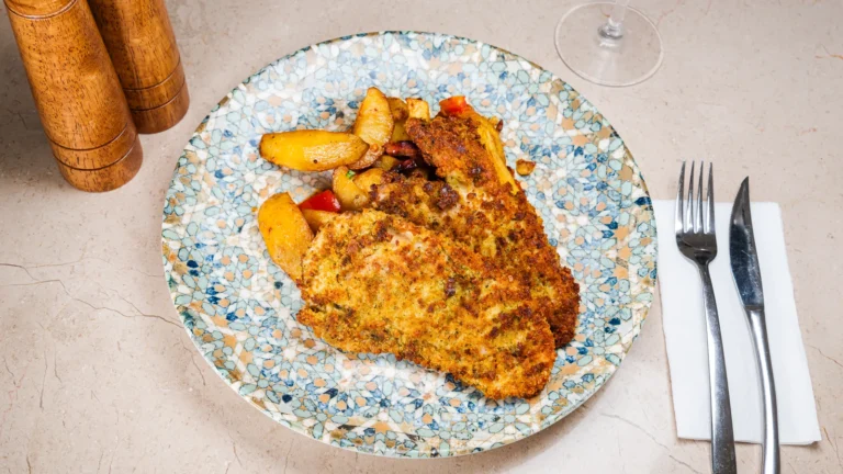 Piept de pui în crustă de parmezan & cartofi cu pancetta și roșii – piept de pui, grana padano, rucola, cartofi. Preparat servit la Restaurant Intim din Focșani