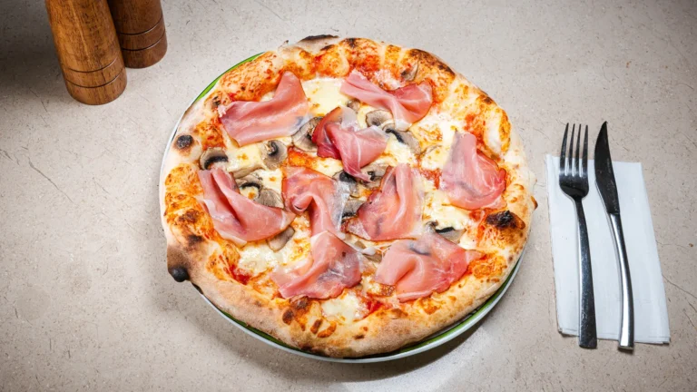Pizza Prosciutto Crudo & Funghi – aluat dospit 24h, sos de roșii, mozzarella, prosciutto crudo. Preparat servit la Restaurant Intim din Focșani