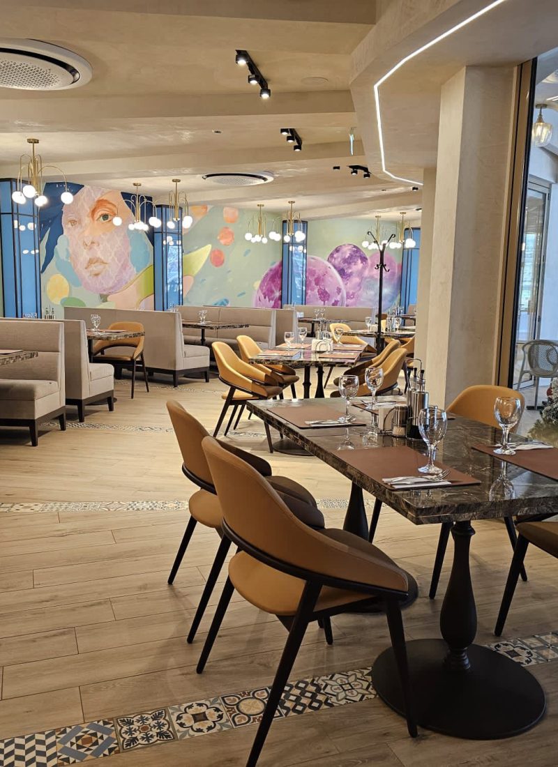 Sala principală a Restaurantului Intim, cu mese pregătite, picturi murale și brad de Crăciun